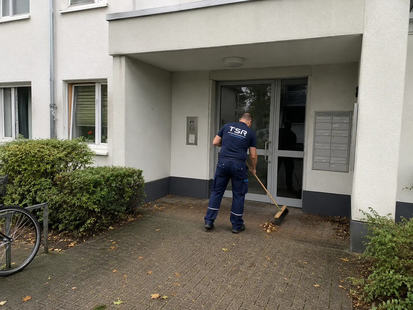 Hauseingang eines Mehrfamilienhauses wird gekehrt