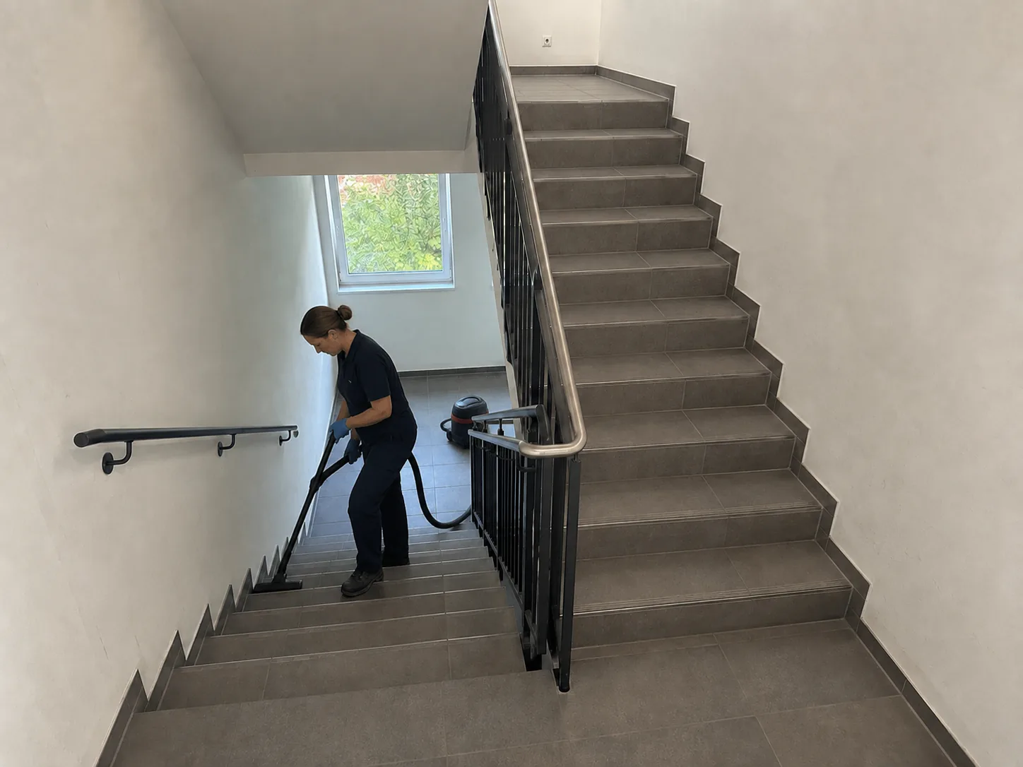 Mitarbeiterin saugt Treppenhausfliesen vor dem Wischen