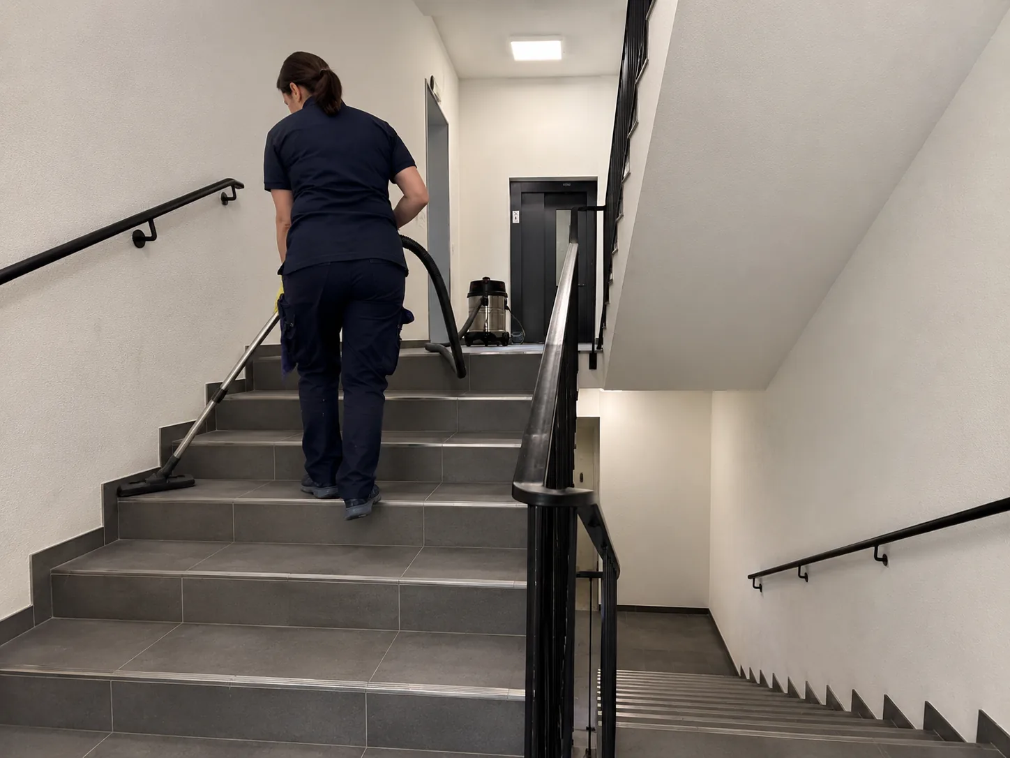 Mitarbeiterin geht mit Staubsauger die Treppe hoch